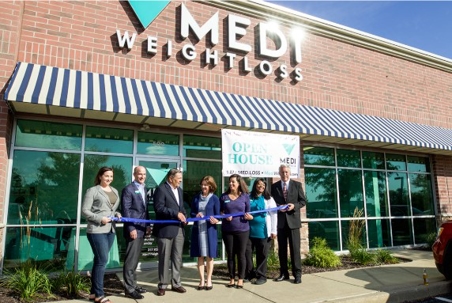 A group of people stands in front of a Medi-Weightloss clinic, cutting a ceremonial ribbon during an outdoor grand opening event. | Medi-Weightloss