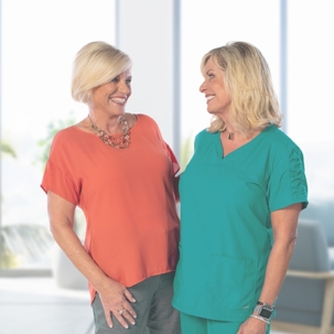 Woman in orange shirt smiling at woman in teal scrubs.