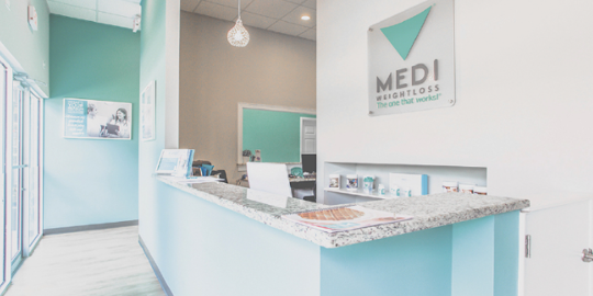 A modern Medi-Weightloss clinic reception area with a sleek front desk, branded signage, and a clean, inviting atmosphere