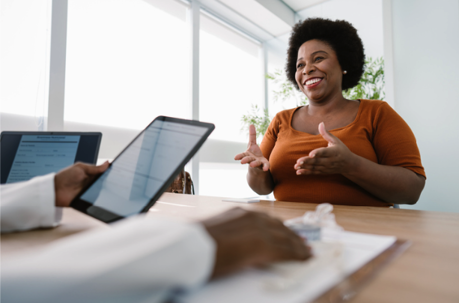 A woman sits across the table from a healthcare provider holding a tablet, discussing her nutritional plan to lose weight. | Medi-Weightloss